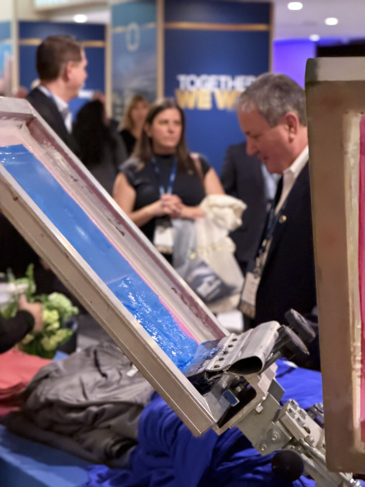 Professional attendees examining screen printing equipment and decorated apparel at an event